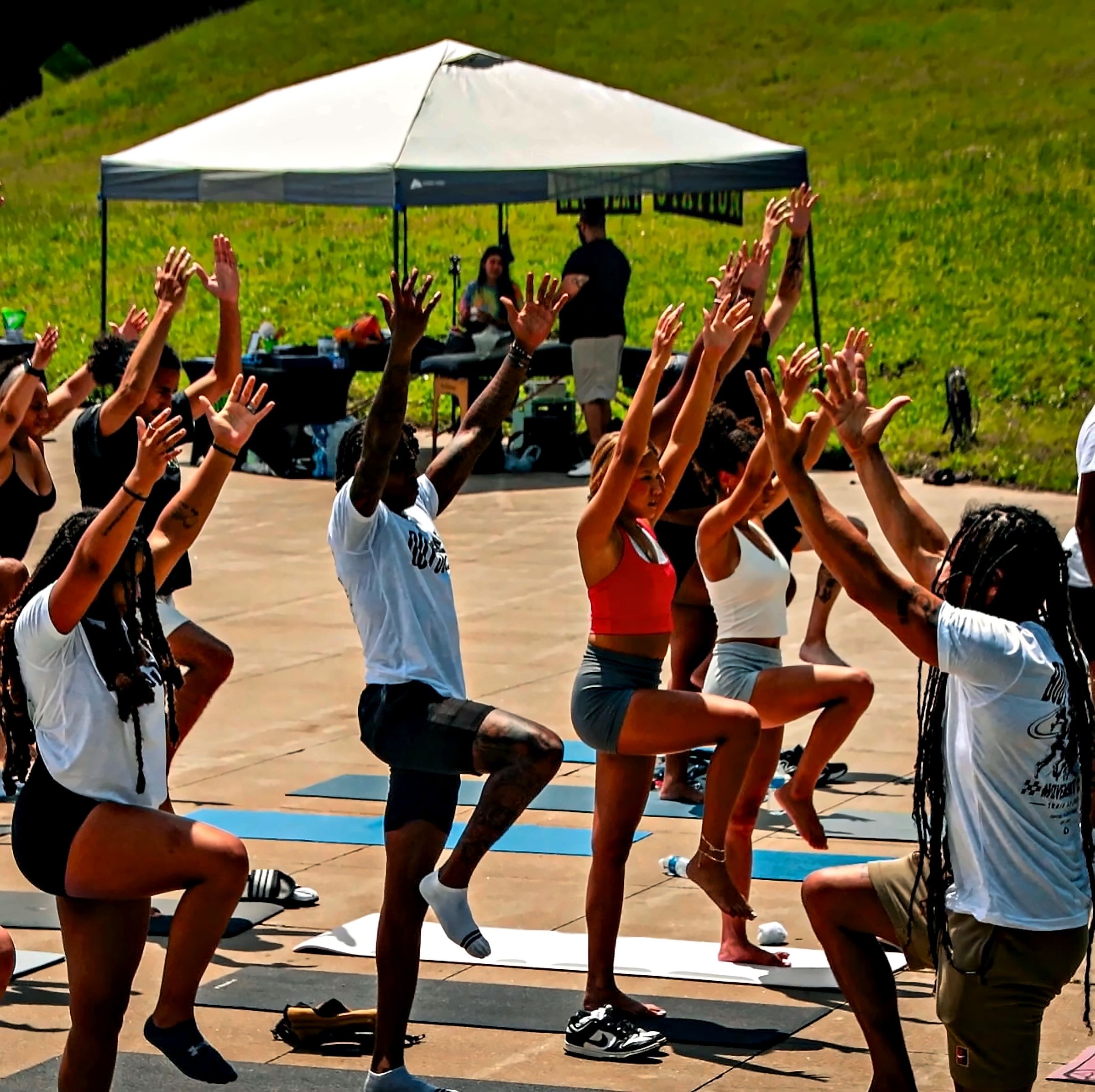 An outdoor group class with arms raised in a balance pose